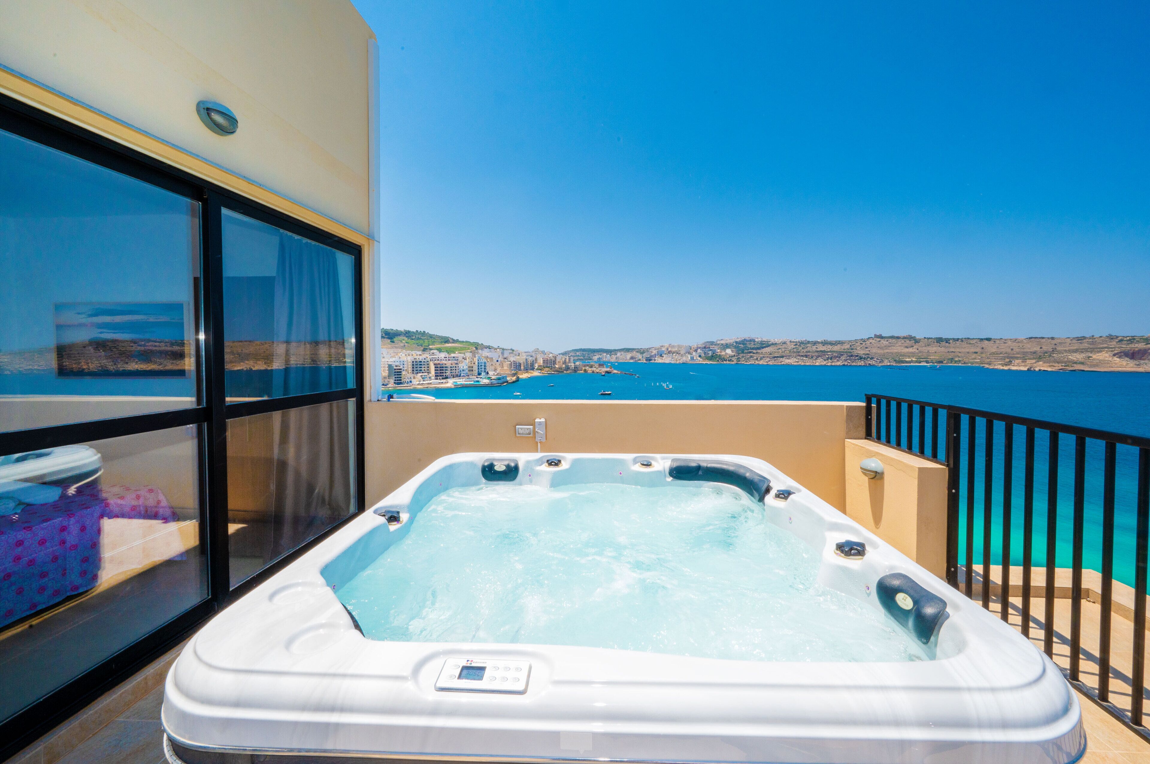 A hot tub on a balcony with a view of the sea and buildings.