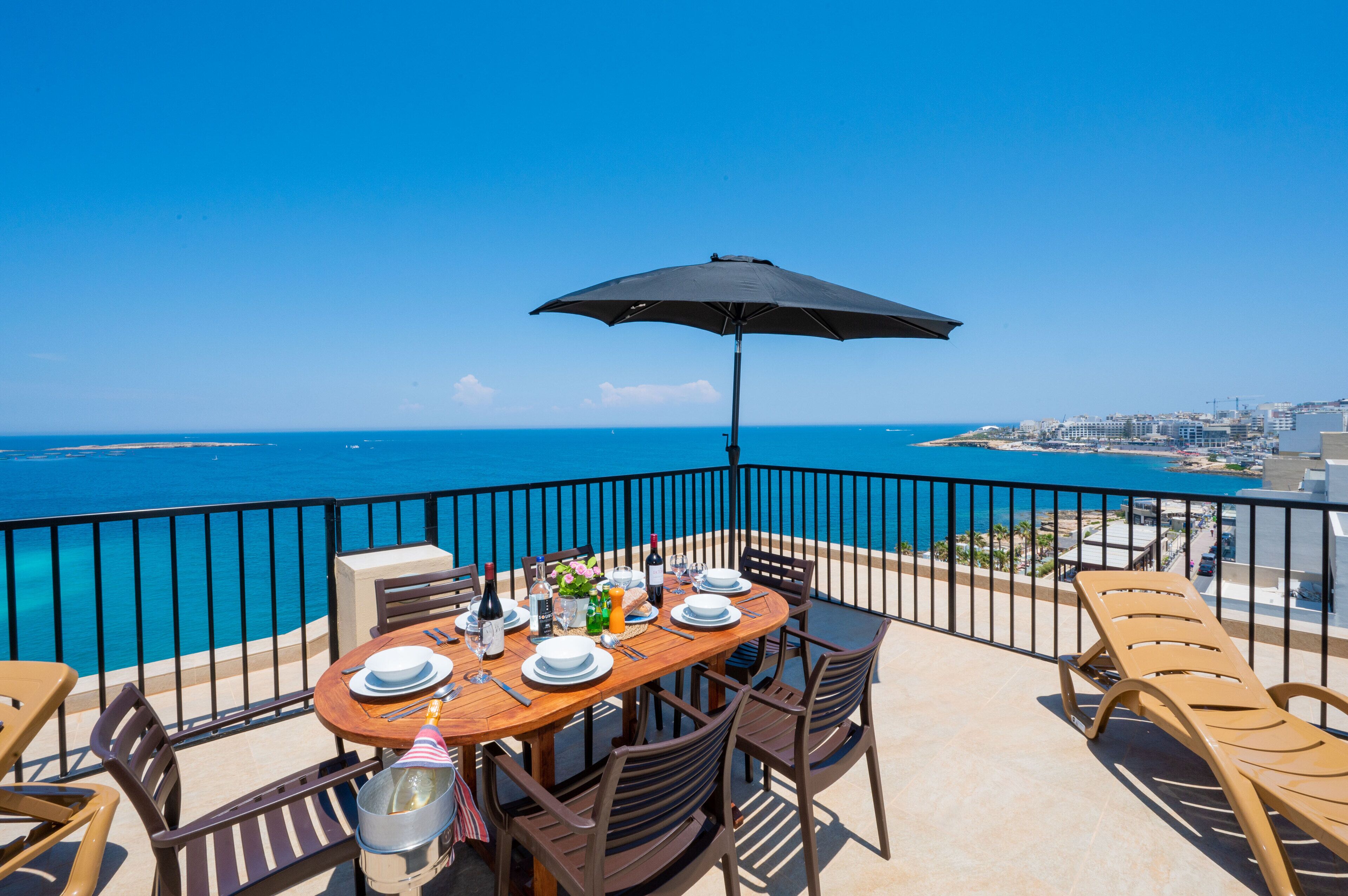 A balcony with a table set for dining, overlooking a coastal cityscape.