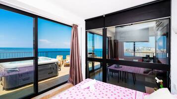 Un balcón con un jacuzzi, una cama con colcha rosa estampada y vista al mar.