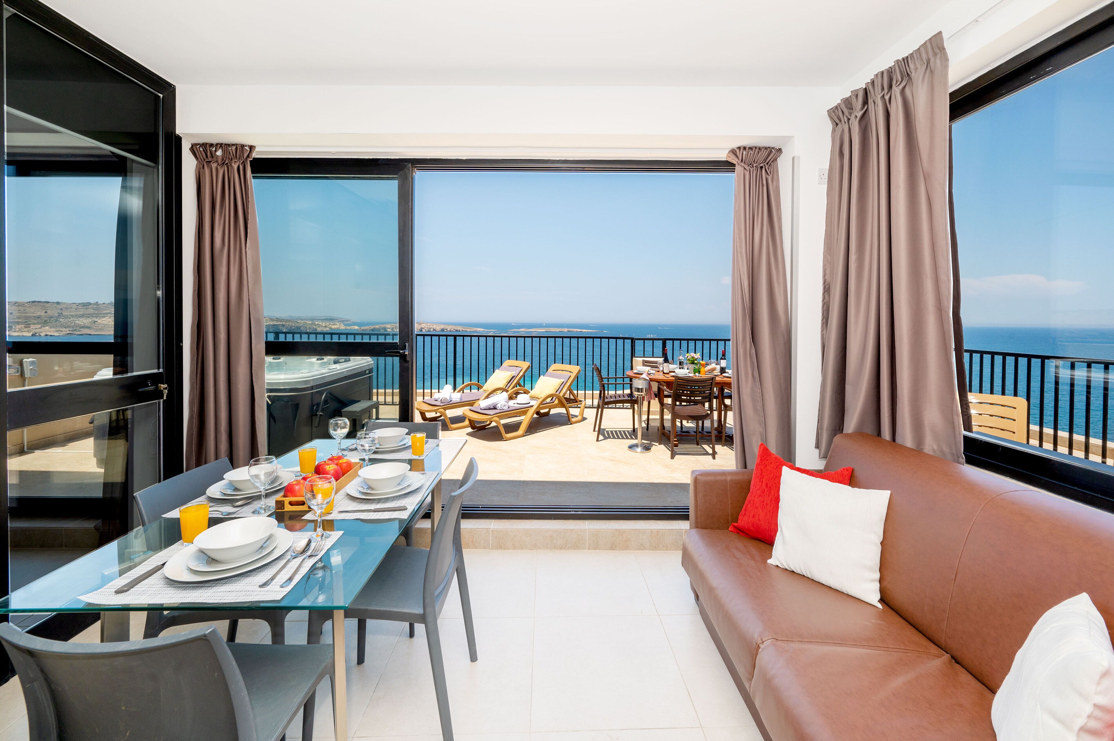 Un balcon avec une table à manger préparée pour le petit-déjeuner, des chaises longues et un canapé agrémenté de coussins.
