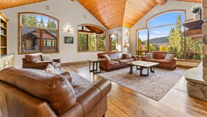 Amplia sala de estar con sofás de cuero, una mesa de centro y ventanas grandes que ofrecen vistas del bosque circundante.