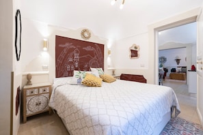 A bedroom with a large bed, a nightstand, a wall clock, and a door leading to another room.