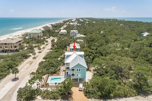 A coastal property with a large house featuring a swimming pool, surrounded by dense greenery and a beach.