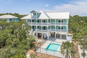 A large, multi-story house with a pool, surrounded by trees.