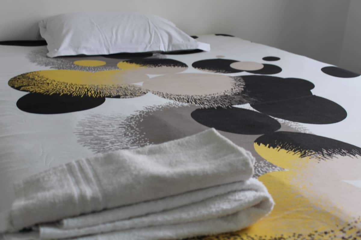 Een bed met een wit kussen en een deken met abstracte zwart-gele patronen.