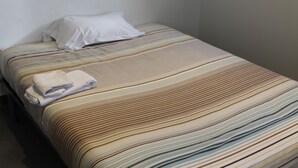 Un lit simple avec une couvre-lit à rayures et une serviette blanche pliée posée dessus.