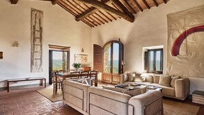 Een ruime woonkamer met een hoge plafond, een grote zithoek, een eettafel met stoelen en uitzicht op het landschap door een groot raam.