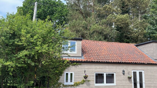 A house with a red-tiled roof, wooden siding, and a front porch with potted plants.