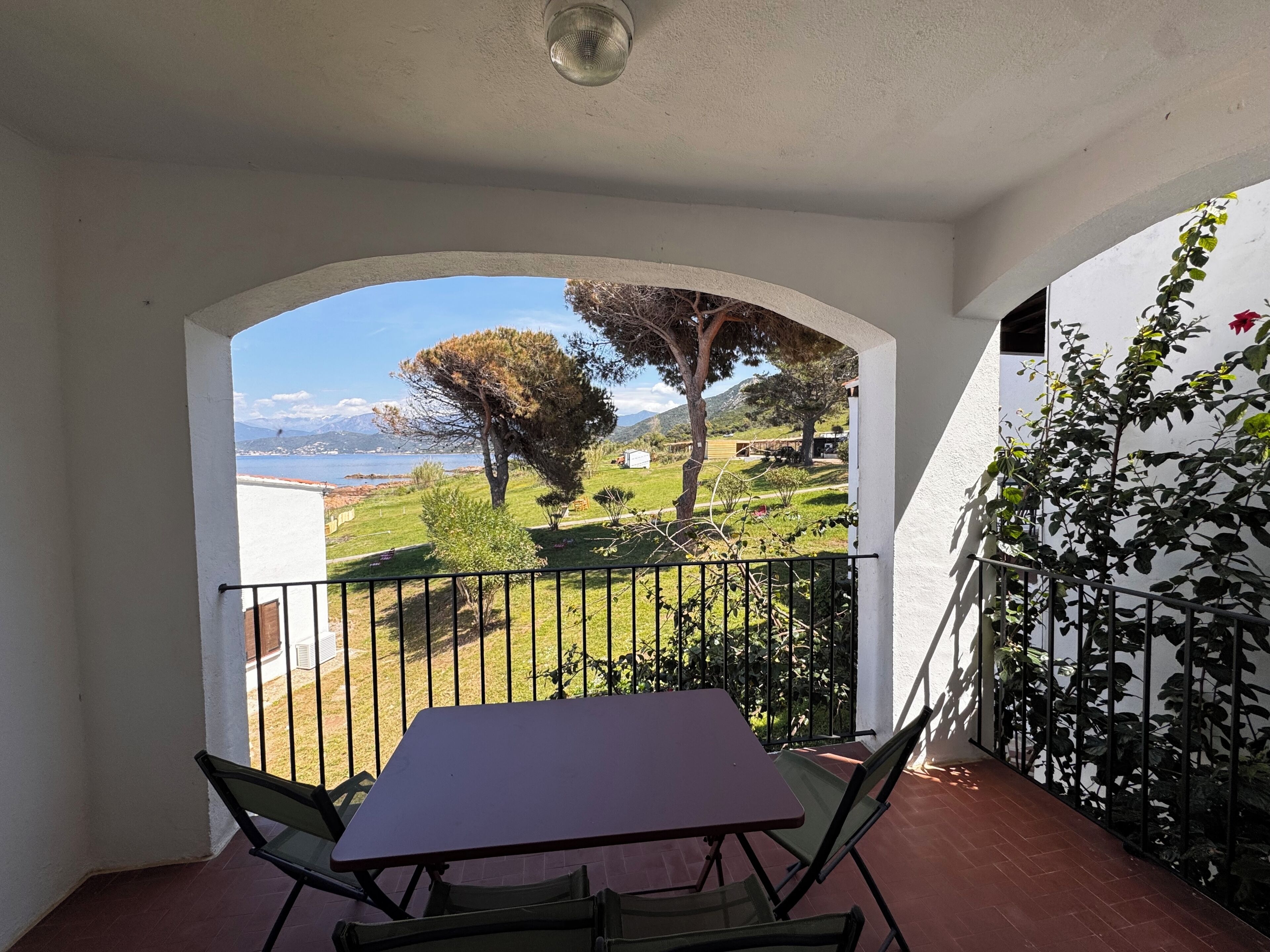 A balcony with a table and chairs, a view of a green landscape, and a clear sky.