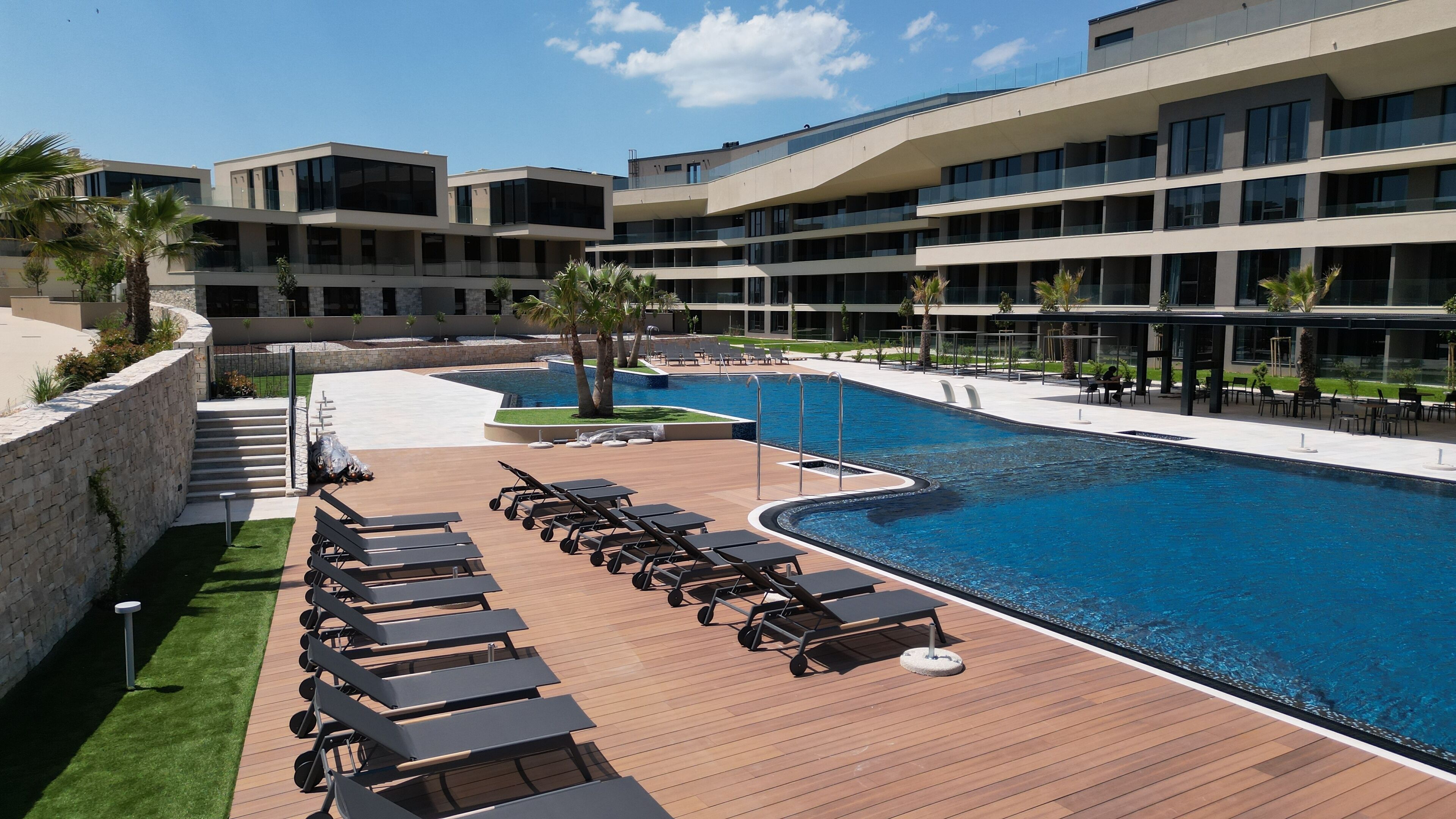 A modern hotel with a large swimming pool, sun loungers, and a landscaped deck area.
