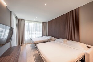 Habitación de hotel con dos camas, un televisor de pantalla plana y un ventanal grande con cortinas.
