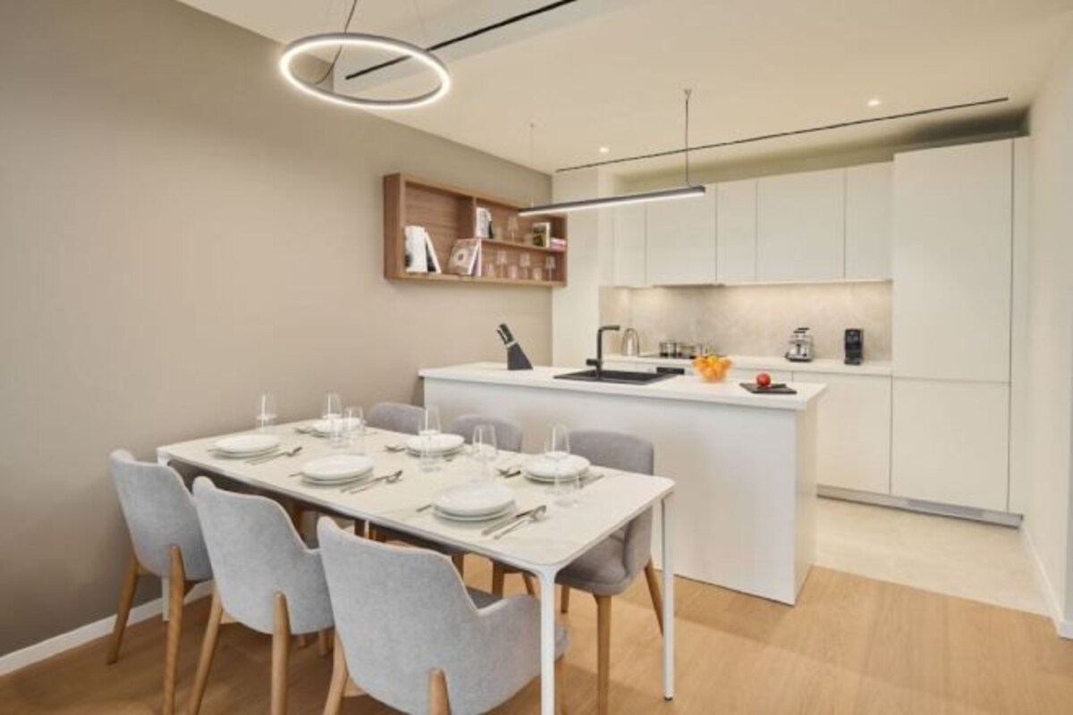 Una cocina moderna con una isla central, muebles blancos y un comedor con una mesa dispuesta para cuatro personas.