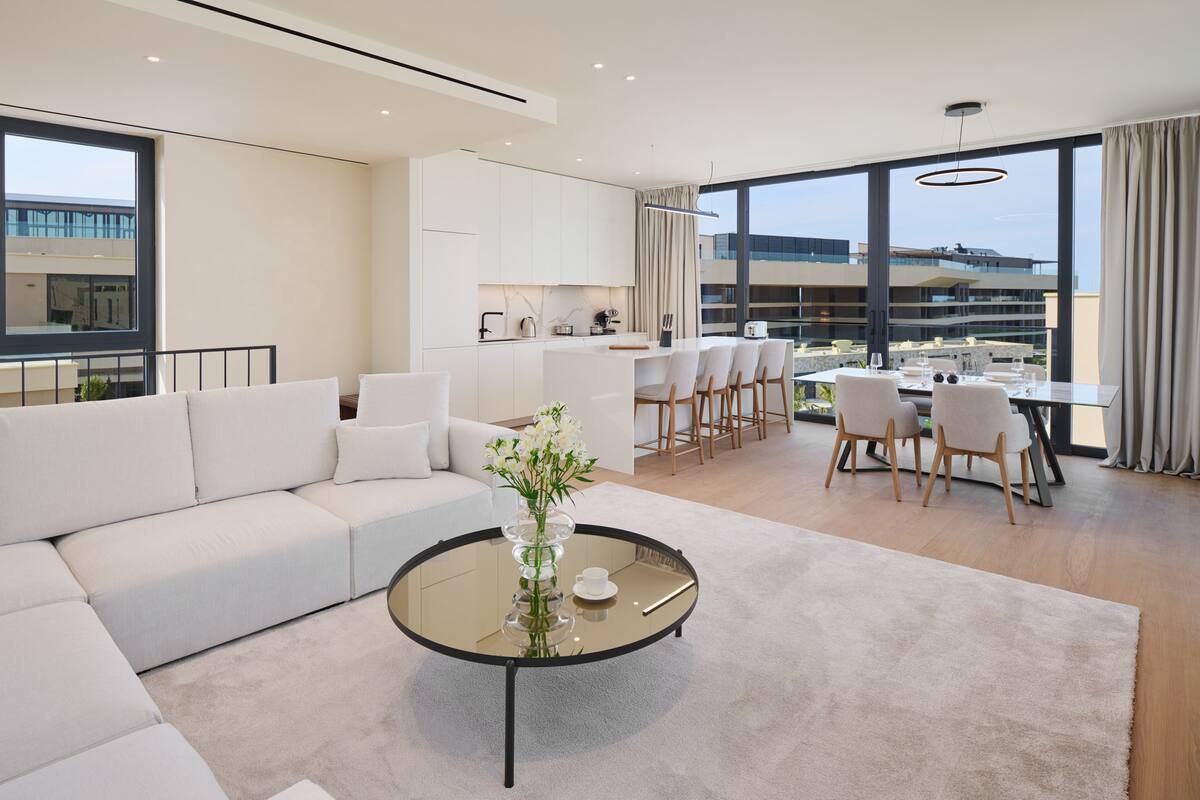 A modern living room with a large sofa, a glass coffee table, and a dining area with chairs and a table.