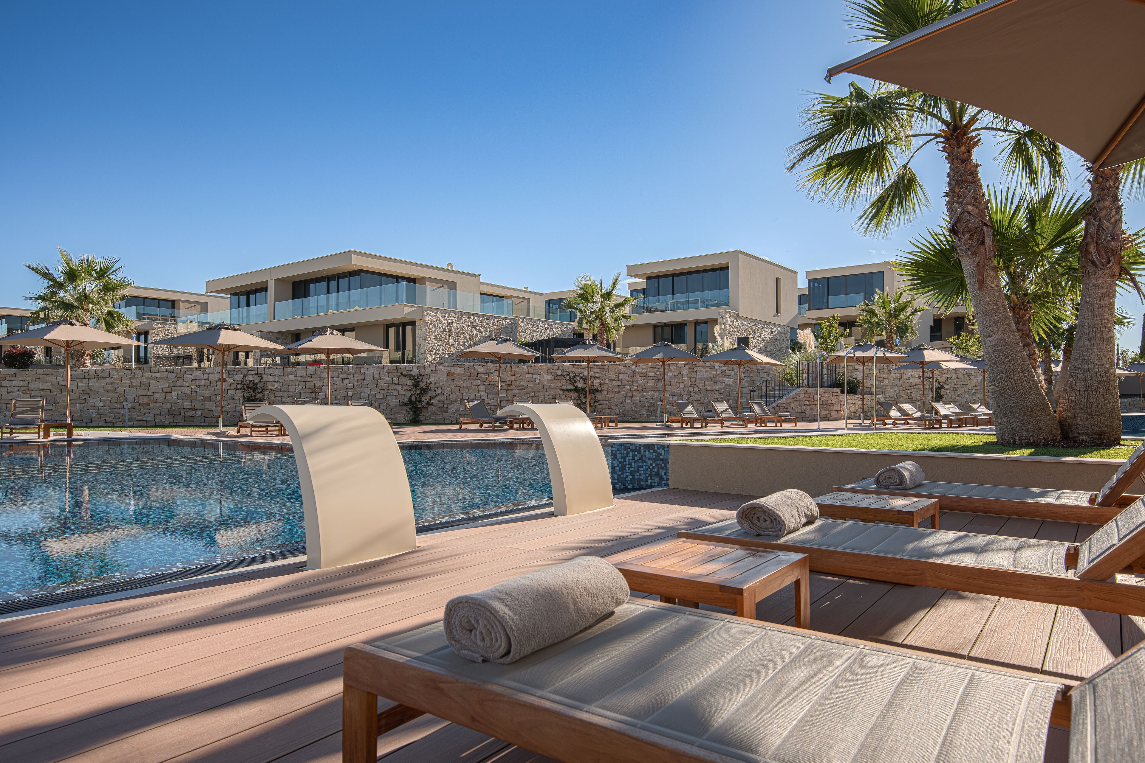 A poolside area with lounge chairs, umbrellas, and a clear view of modern buildings in the background.