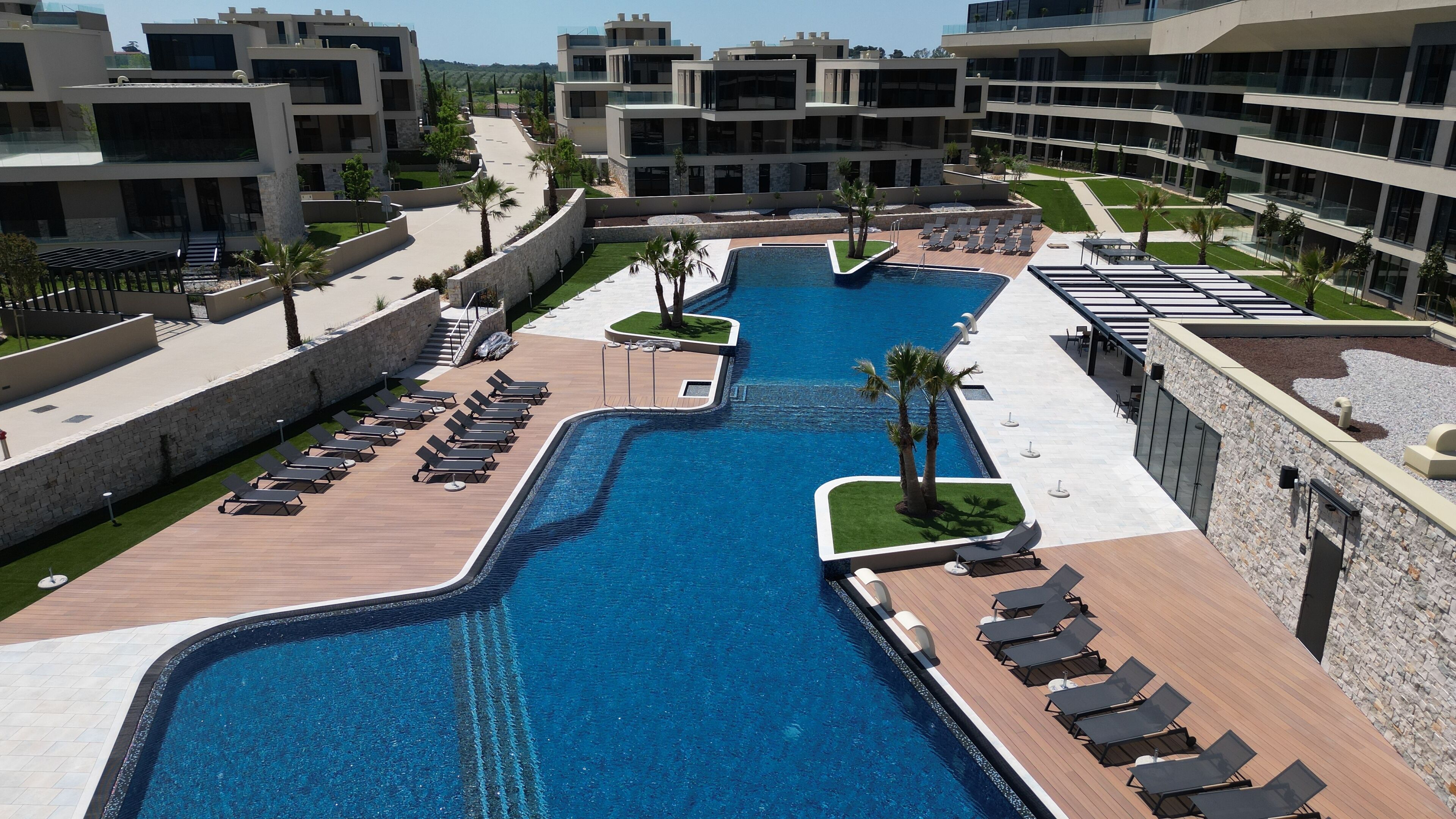 Een modern hotel met een centraal gelegen zwembad, ligbedden en een goed onderhouden tuin.