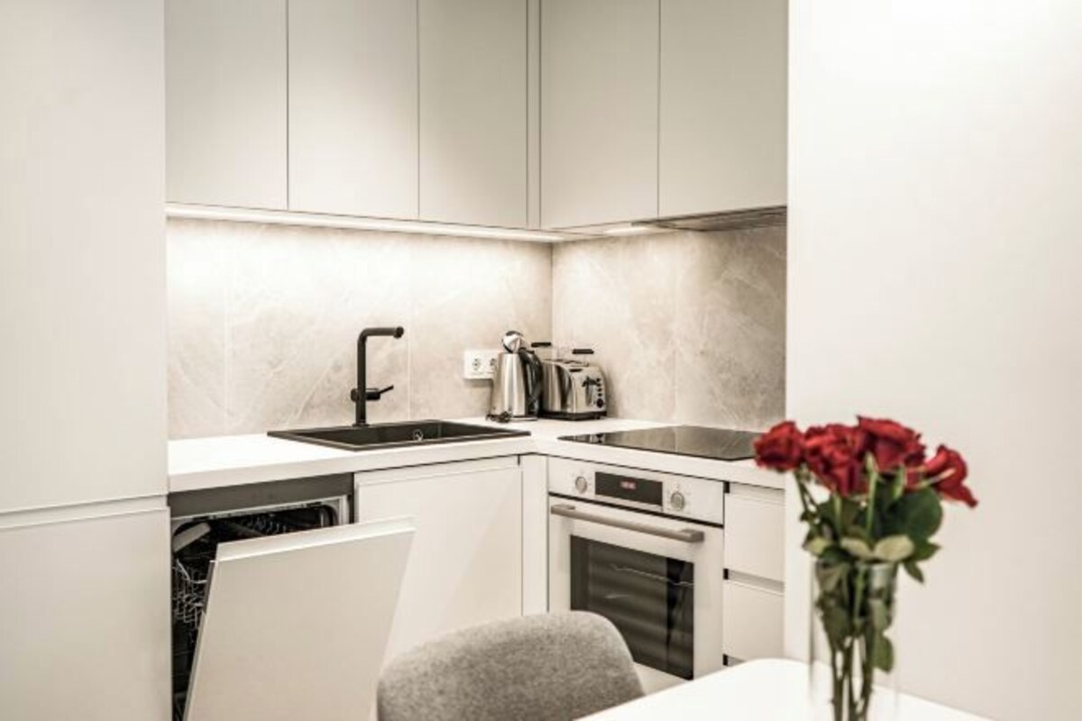 Una cocina moderna con un lavamanos, estufa y lavavajillas, y un comedor con una silla y un jarrón de flores.