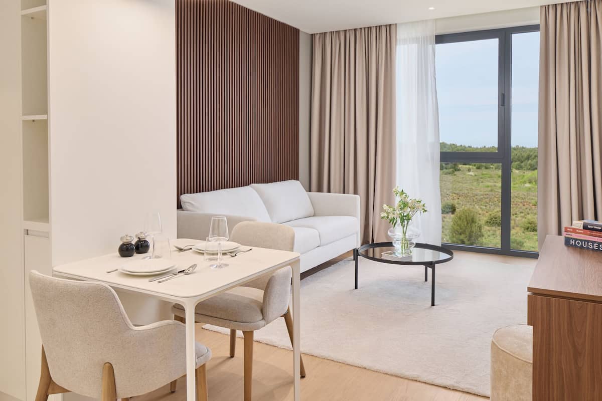 A modern living room with a dining area, a sofa, a coffee table, and a view of the outdoors.