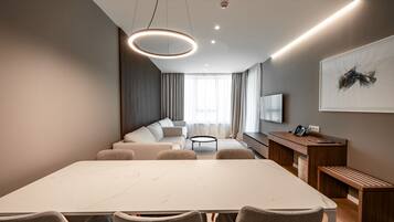 A modern hotel room with a large marble dining table, a sofa set, a wooden desk, and a large abstract painting on the wall.