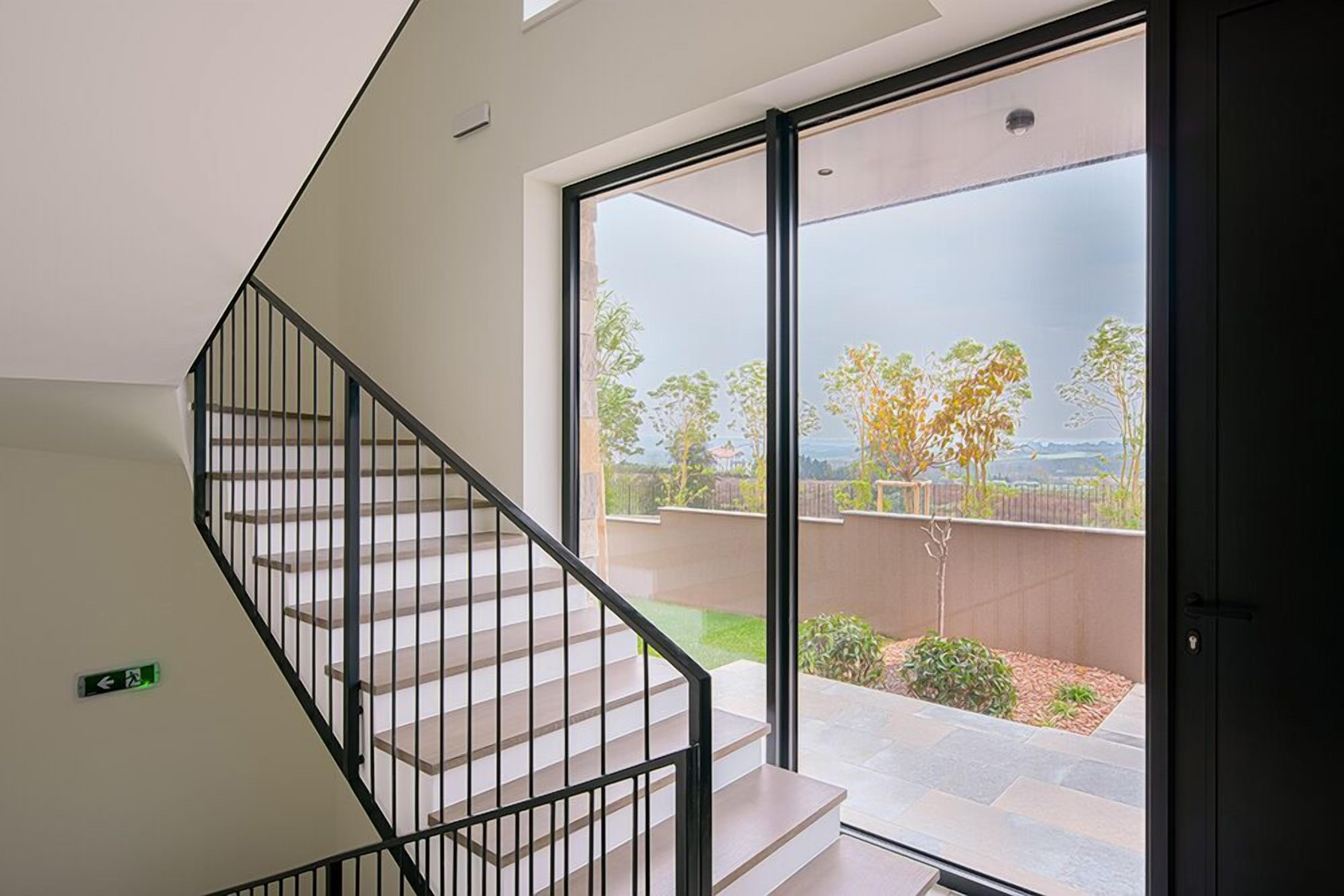 A modern staircase with a glass door leading to an outdoor patio with a view of trees and a fence.