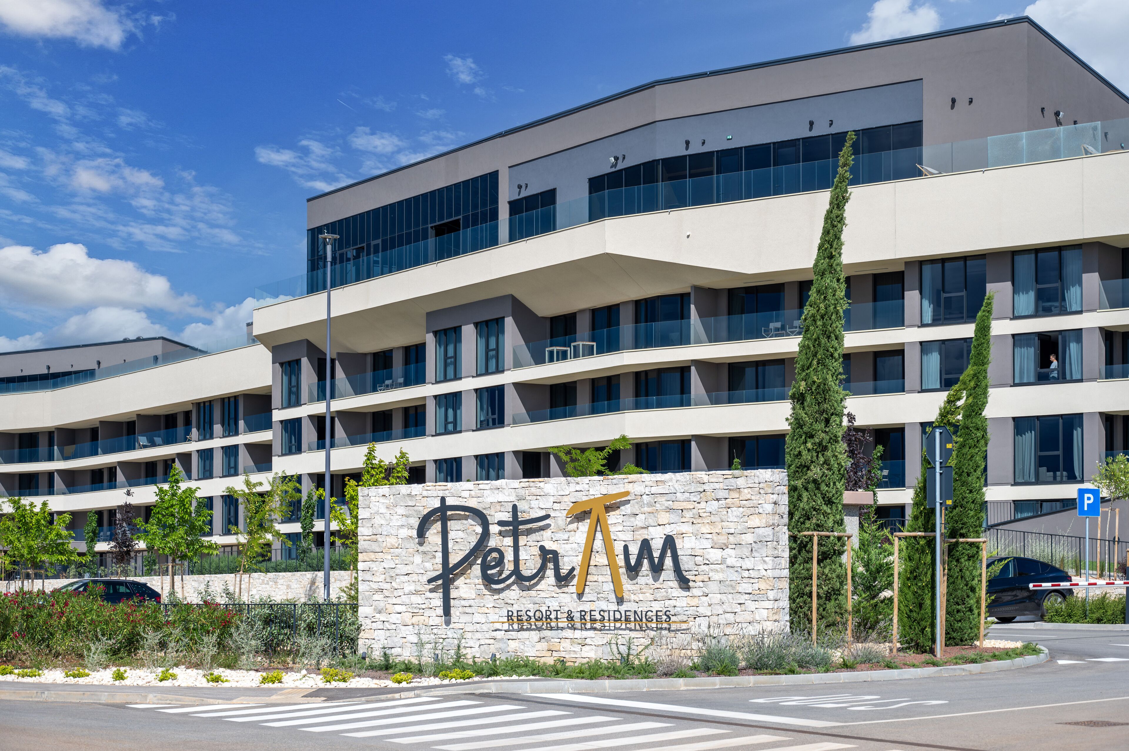 A modern building with a sign reading "PetrTm Resort & Residences" and a parking sign.