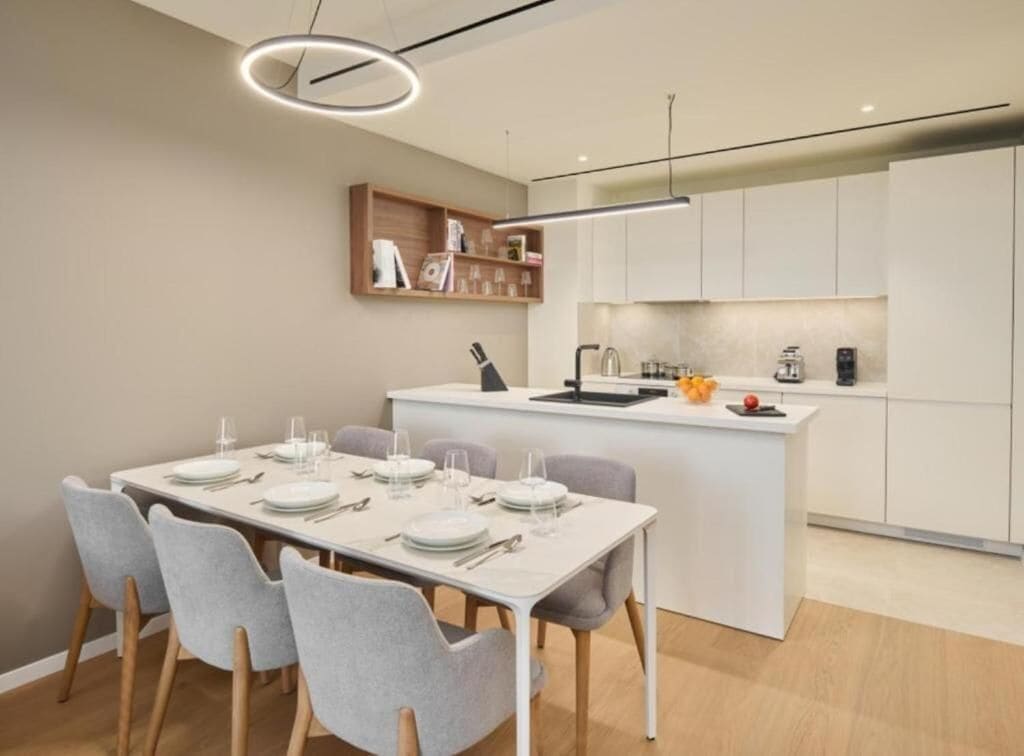 Una cocina moderna con armarios blancos, una isla central con lavamanos y un comedor con mesa para cuatro.