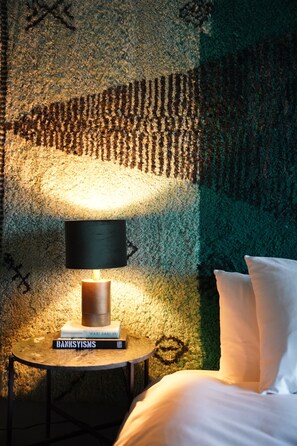 A bed with white pillows, a round side table with a lamp, and a book titled "BANKSYMSIS" on the table. - EDVILLE HOME GHENT (Melle)