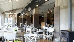 A modern restaurant with white chairs and tables, exposed brick walls, and pendant lighting. - NAOUSSA MOUNTAIN RESORT (Naousa)