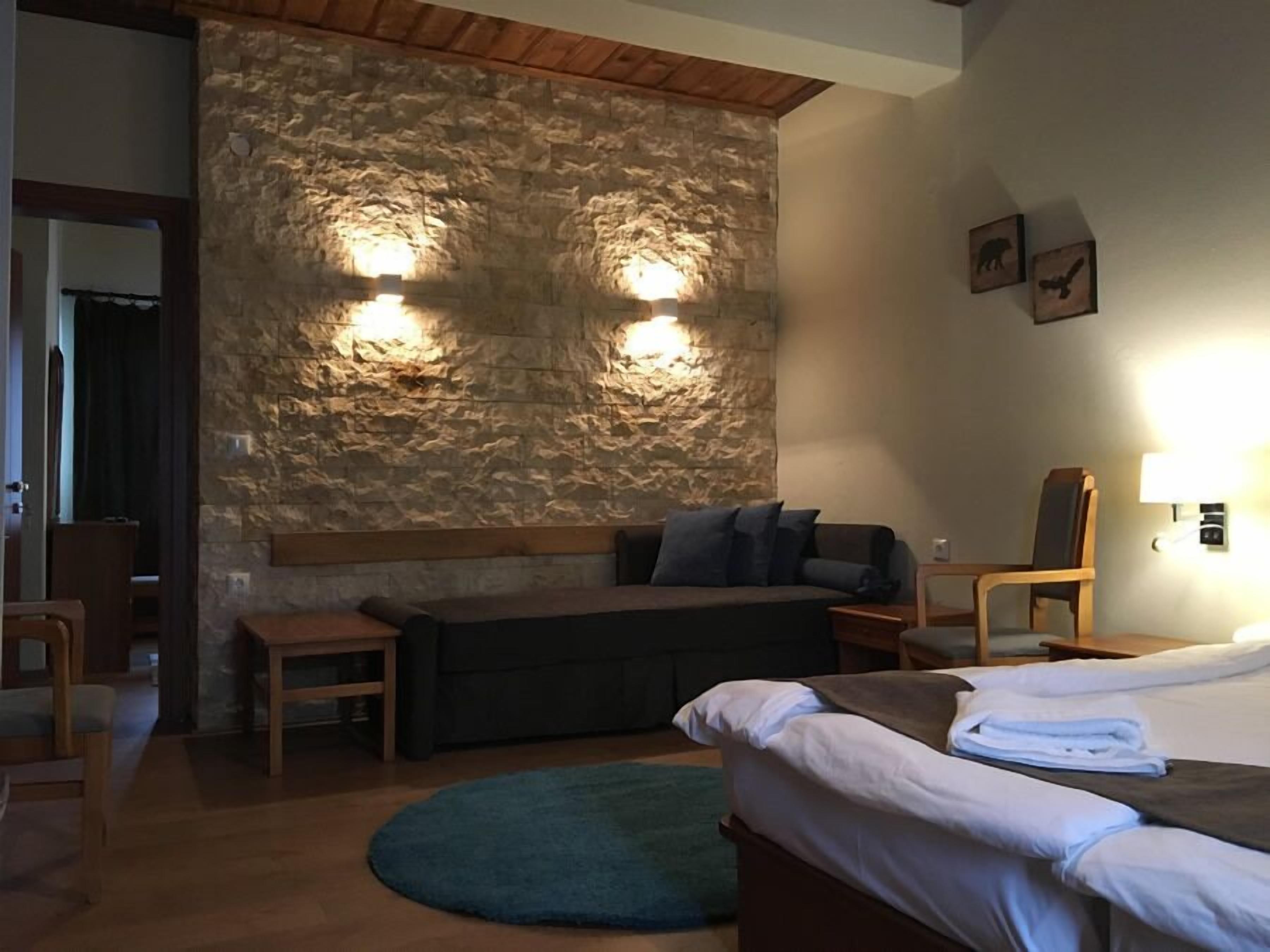 A cozy room with a stone wall, a bed, a sofa, and a chair.