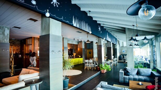 A modern hotel lobby with a seating area, a reception desk, and a dining space. - NAOUSSA MOUNTAIN RESORT (Naousa)