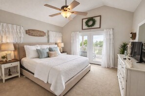 A bedroom with a bed, nightstands, a ceiling fan, a television, and a balcony with a view.