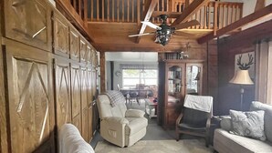 Ein geräumiges Wohnzimmer mit hohen Decken, Holzbalken, einem Deckenventilator und Blick auf einen Essbereich.