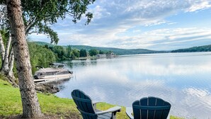 Two Adirondack chairs facing a calm lake with a dock and a house in the background. - Private Lakefront Cabin (Eagle Lake)