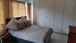Un dormitorio con cama, mesita de noche, lámpara, armario y ventana con cortinas.