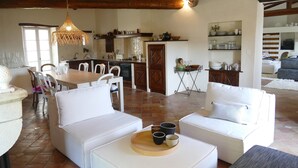 Ein ger äumiges Wohnzimmer mit weißen Sofas, eine Essecke mit Holztisch und eine Küche mit weißen Schränken und einer Pendelleuchte.