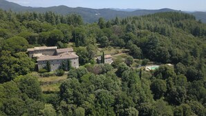 Ein aus Stein gebautes Haus mit Ziegeldach, umgeben von dichtem Wald, mit Bergen im Hintergrund.