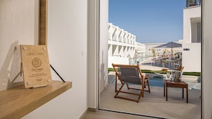 Een moderne hotelkamer met een glazen deur naar een zwembadgedeelte, een houten plaquette aan de muur en een kleine tafel met een stoel.