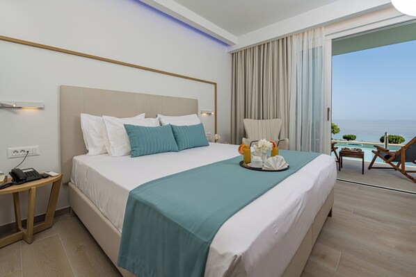A hotel room with a large bed, a bedside table with a phone, a small table with a tray of breakfast items, a chair, and a view of the ocean. - Mirage Bleu Hotel (Zakynthos)