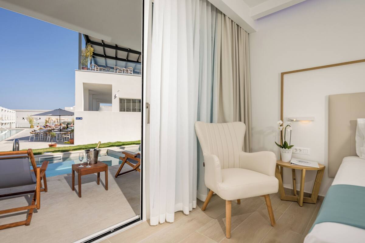 Habitación de hotel con cama, una silla, una mesita y vistas a la piscina y al área exterior.
