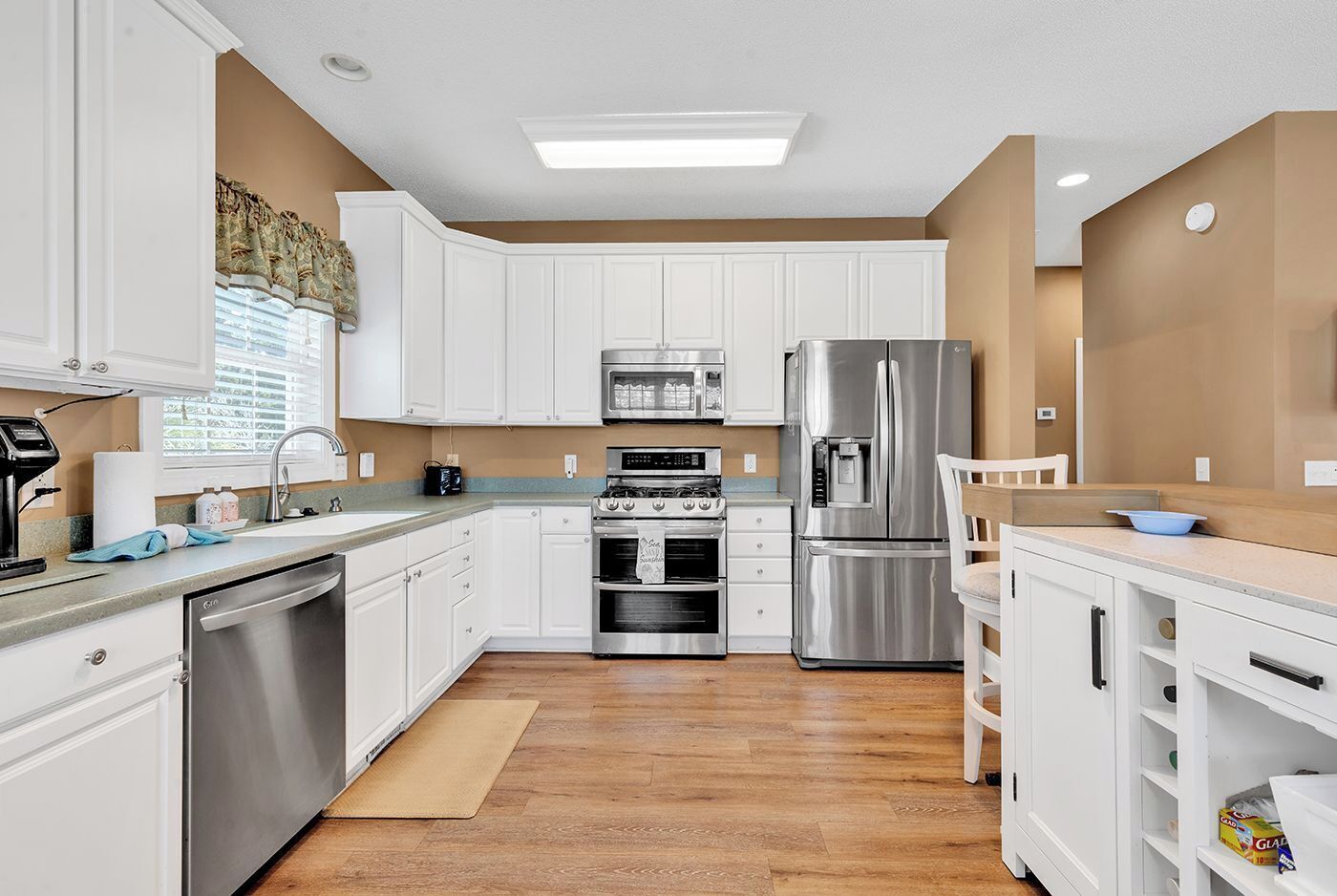 Une cuisine moderne avec des meubles blancs, des appareils en acier inoxydable et un plancher en bois.