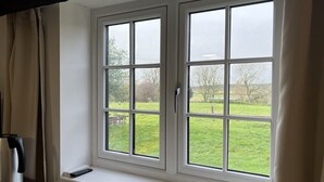 A room with a large window overlooking a grassy area. - Tumbleweed Cottage (Newark)