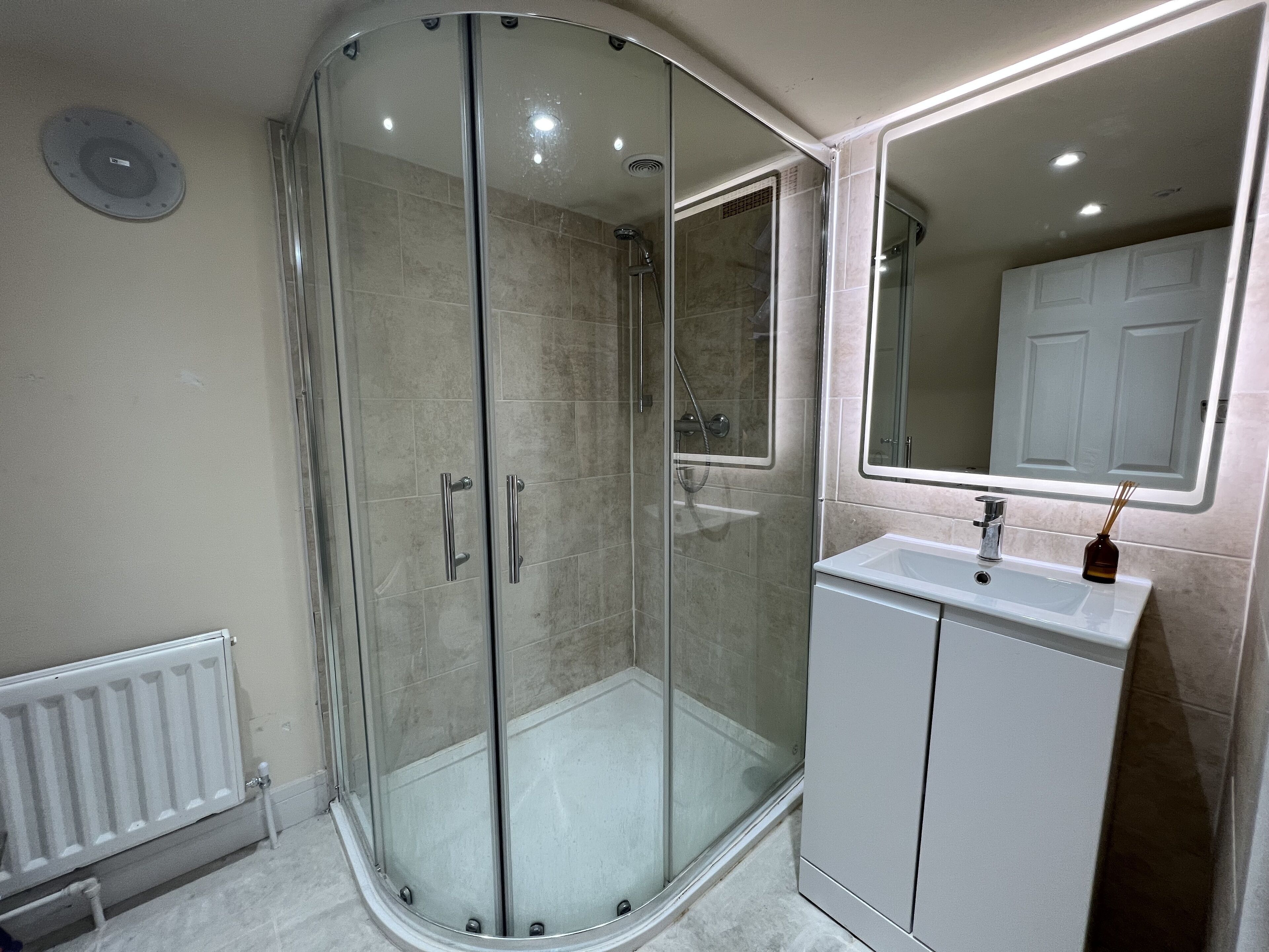 A modern bathroom with a glass-enclosed shower, a white sink, and a mirror above it.