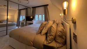 A bedroom with a large bed, a television, a desk, and a window with curtains. - Tumbleweed Cottage (Newark)