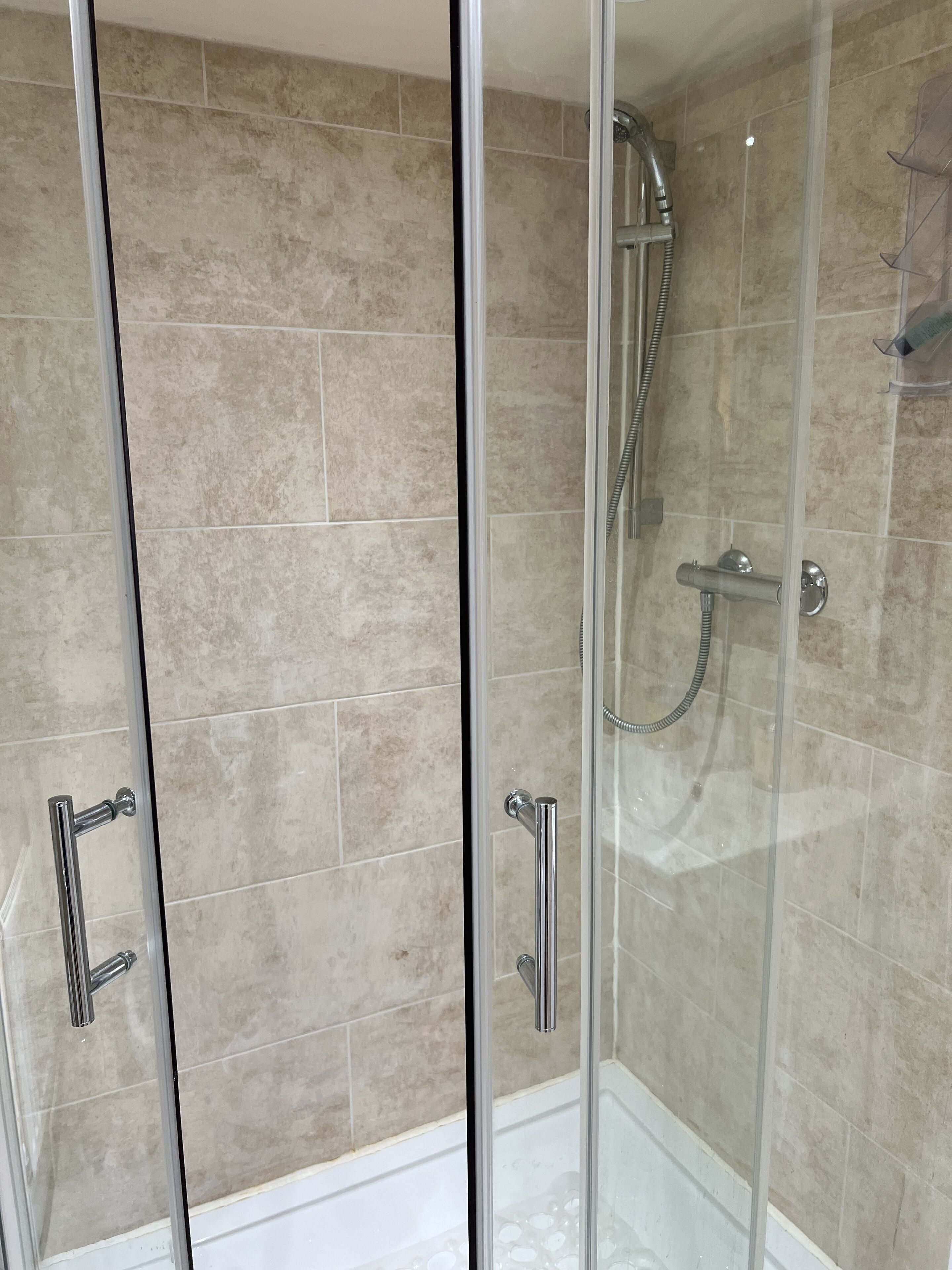 A glass-enclosed shower area with beige tiles and chrome fixtures.