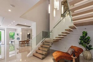 Un intérieur moderne avec un escalier en verre, un coin repas et un espace de vie agrémenté d’une plante et d’un canapé.