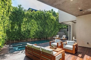 A modern outdoor pool area with wooden furniture and a lush green wall.