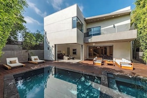 A modern two-story house with a swimming pool, outdoor seating, and a large glass door entrance.