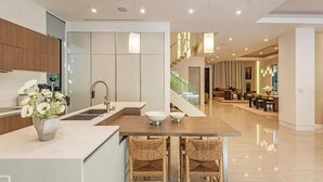 Une cuisine moderne dotée d’un îlot central, un coin repas avec un escalier, et un espace de vie offrant une vue dégagée.