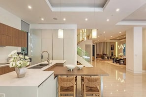 A modern kitchen with a central island, a dining area with a staircase, and a living space with a view. - Harper - Unparalleled Luxury Living in a Contemporary Modern Villa (Los Angeles)