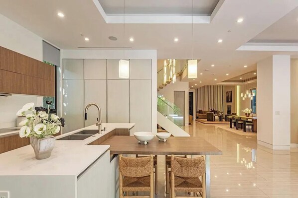 A modern kitchen with a central island, a dining area with a staircase, and a living space with a view.