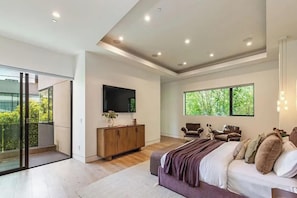 A modern bedroom with a large bed, a TV, a wooden cabinet, and a balcony with glass doors.